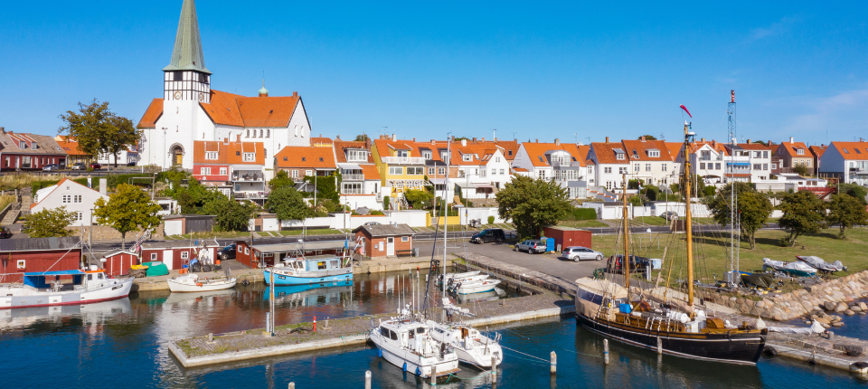 Blick auf den Hafen von Rønne auf Bornholm mit Booten, roten Ziegeldächern und der markanten Kirche vor blauem Himmel.