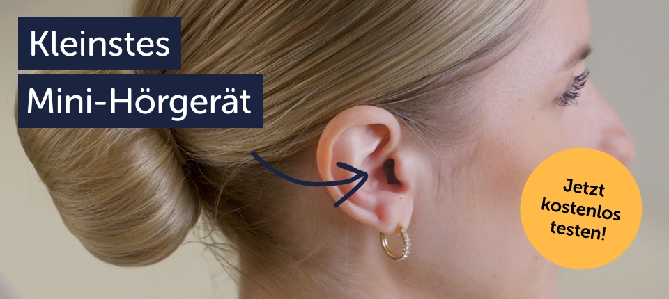 Nahaufnahme einer Frau mit hochgesteckten Haaren, die ein nahezu unsichtbares, schwarzes Mini-Hörgerät im Gehörgang trägt.